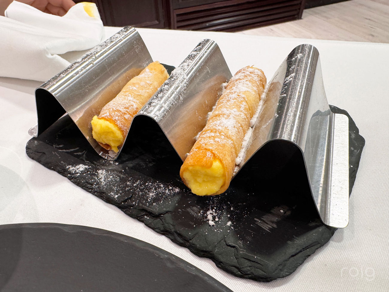 Postre gourmet servido sobre soporte metálico ondulado con base de pizarra negra en restaurante El Mosquito